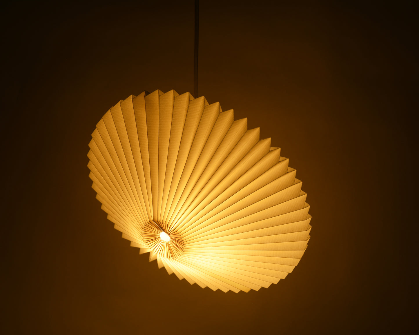 Handcrafted white origami paper lamp in the shape of a flying saucer, featuring delicate pleats and casting a warm, mood-lighting glow.