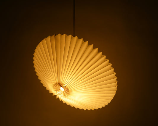 Handcrafted white origami paper lamp in the shape of a flying saucer, featuring delicate pleats and casting a warm, mood-lighting glow.